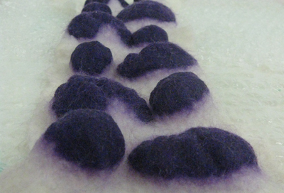 Felting partial felt shapes into a thin background of fiber and using circumferential fulling to shrink the thinner wool around the base of the Partial Felts causing the shapes to dome (Pam Wittfeld’s work, Arrowmont School of Crafts, Gatlinburg, TN workshop, 2012).
