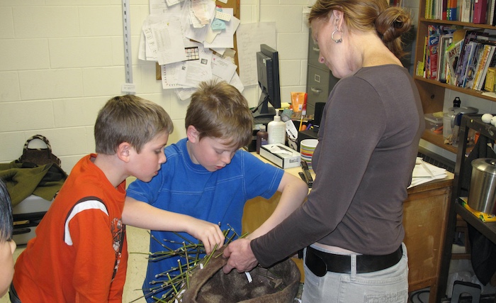 Students weaving locally harvested branches in and out of holes in the nest as mother birds work twigs into their nest with their beaks