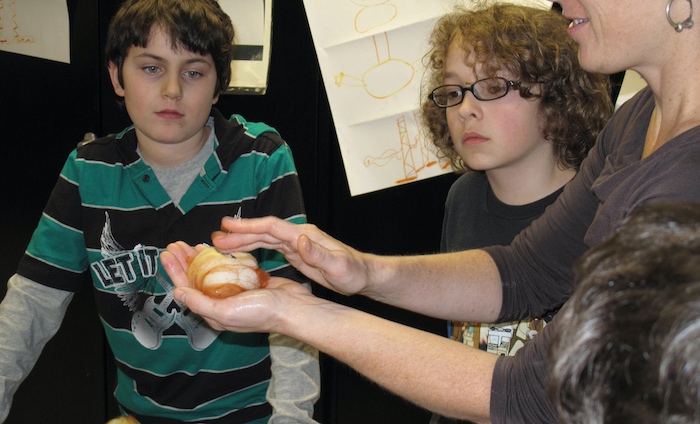 Demonstrating the gentle agitation needed to coerce the wool fibers through the students' silk name tags to secure them to the surface of the felt skin